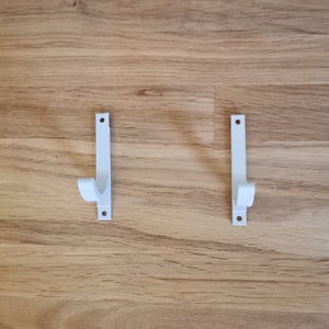 May include: Two white plastic wall mounted hooks with a curved design.