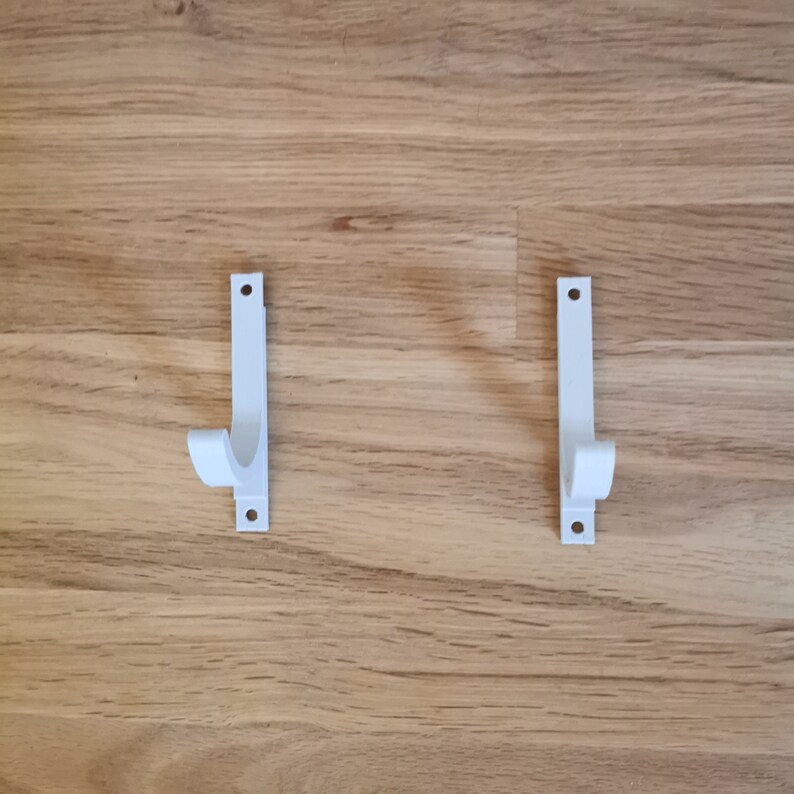 May include: Two white plastic wall mounted hooks with a curved design.