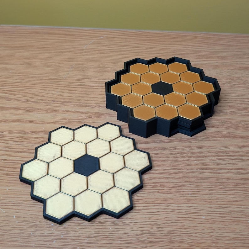 May include: A black and gold honeycomb-shaped coaster set. The coaster is made of multiple layers of honeycomb-shaped tiles. The tiles are black on the outside and gold on the inside.