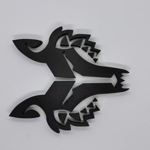 May include: A black, stylized wolf head design, with intricate details and a sharp, angular shape. The design is made of a solid material, possibly wood or plastic, and has a smooth, matte finish.