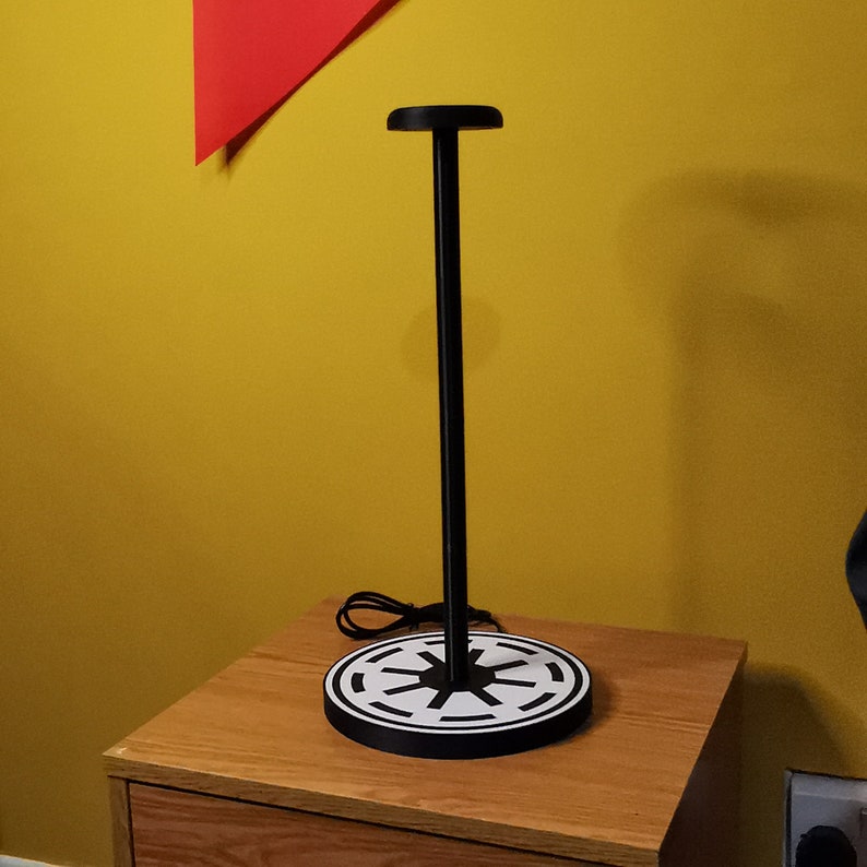 May include: A black metal headphone stand with a round base featuring a white and black imperial symbol.