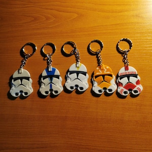 May include: Five keychains featuring different colored Star Wars Clone Trooper helmets. Each keychain has a silver chain and a silver ring.