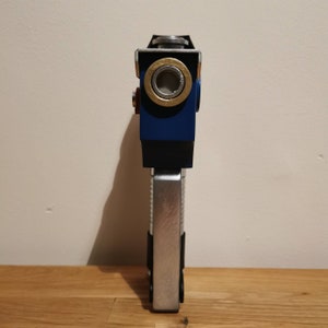 May include: A blue and silver toy gun with a round, silver barrel and a black handle. The gun has a gold ring around the barrel.