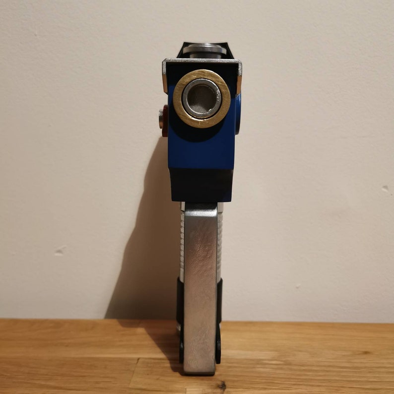 May include: A blue and silver toy gun with a round, silver barrel and a black handle. The gun has a gold ring around the barrel.