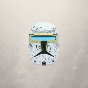 May include: A white and yellow plastic helmet with a black visor and a pattern of small black stitches. The helmet is a replica of a Star Wars clone trooper helmet.