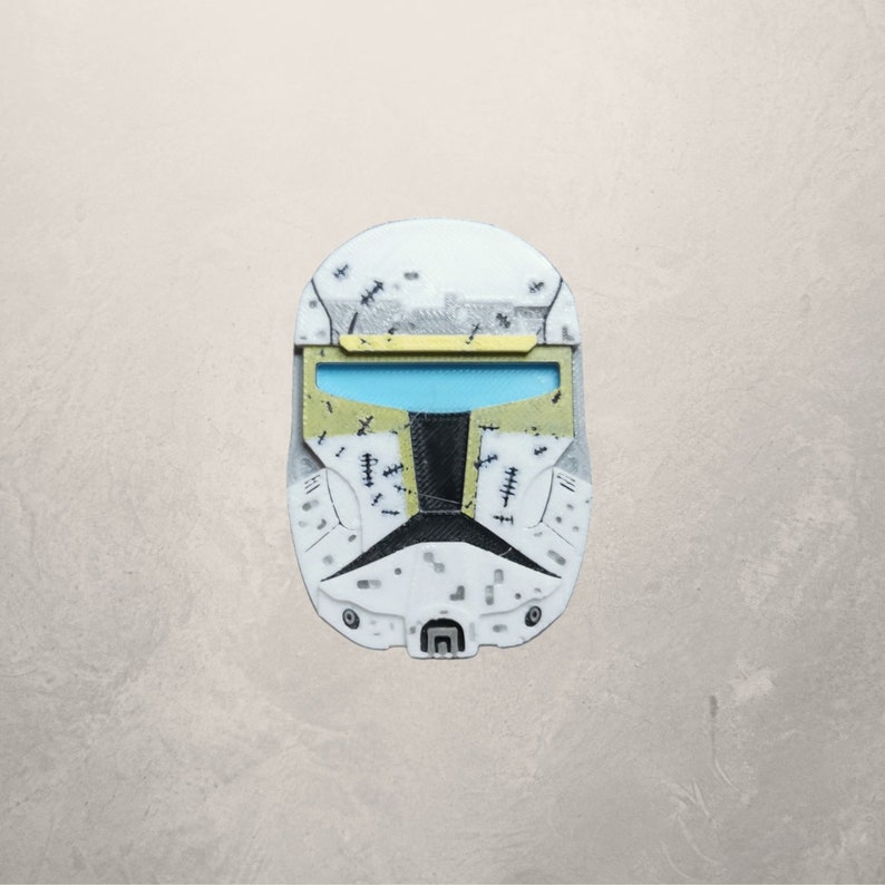 May include: A white and yellow plastic helmet with a black visor and a pattern of small black stitches. The helmet is a replica of a Star Wars clone trooper helmet.