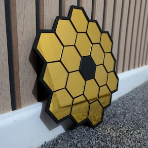 May include: A gold mirror with a honeycomb design. The mirror is made of many small hexagonal mirrors that are arranged in a circular pattern. The mirror is surrounded by a black frame.