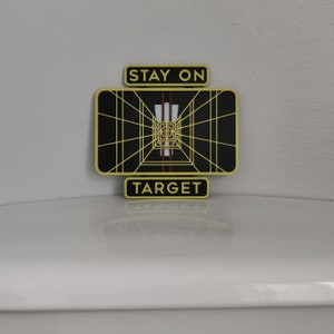 May include: A yellow and black Star Wars themed target sign with the text "Stay on Target".