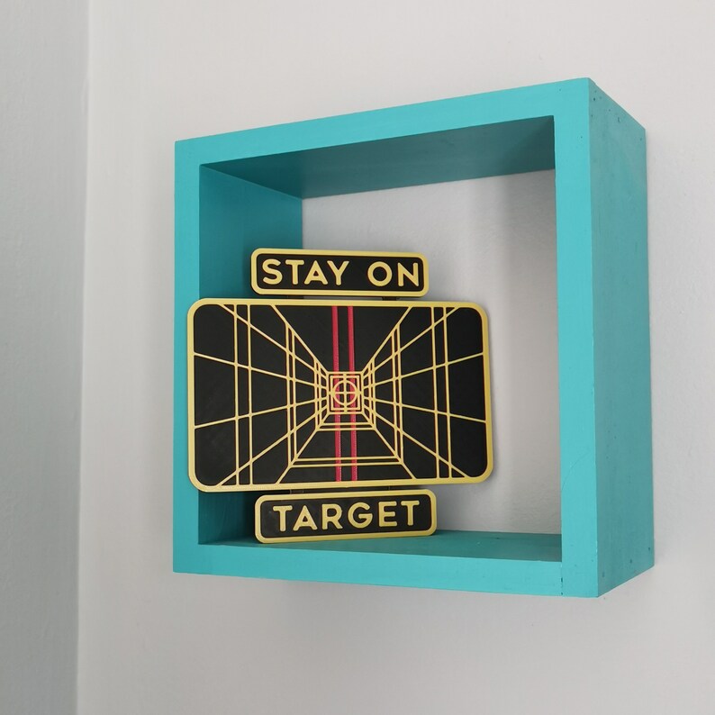 May include: A turquoise wooden shelf with a black and gold framed image that says "Stay on Target". The image is a black and white graphic of a tunnel with red lines.