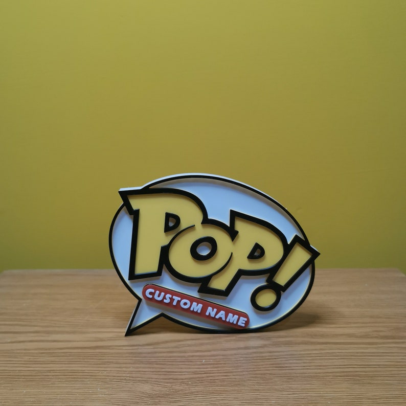 May include: White and yellow 3D printed Pop! logo with black outlines. The logo is in the shape of a speech bubble with the word "Pop!" in all caps and the text "CUSTOM NAME" below it.