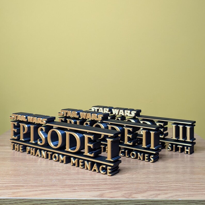 May include: Three black and gold Star Wars Episode titles. The first title is "Episode I The Phantom Menace", the second is "Episode II The Clones", and the third is "Episode III Sith".