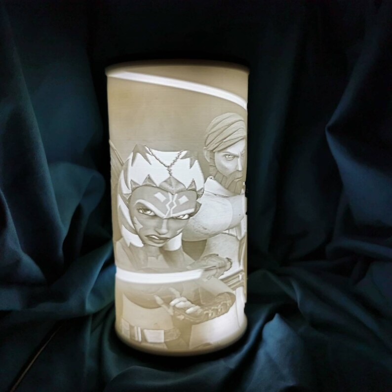 May include: A white ceramic lamp with a 3D printed design of two Star Wars characters, Ahsoka Tano and Anakin Skywalker. The lamp is lit and the design is visible.