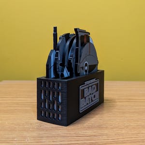 May include: A black and gray Star Wars: The Bad Batch themed coaster set with a black stand. The coasters feature various characters and vehicles from the show.