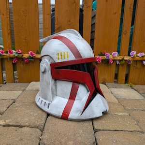 May include: A white and red plastic helmet with a black visor and yellow stripes. The helmet has a red and white stripe pattern.