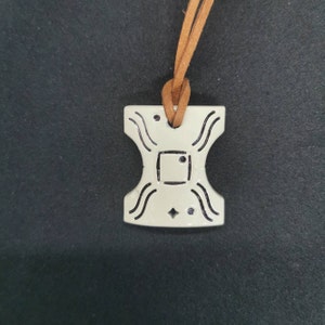 May include: A white ceramic pendant with a geometric design, featuring a square in the center and a brown leather cord.