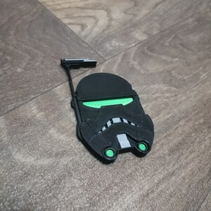 May include: A black and green 3D printed Star Wars Stormtrooper helmet with a raised design. The helmet has a green visor and green eyes.