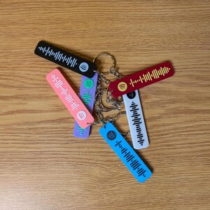 May include: A set of six colorful keychains with a barcode-like design and a small circle in the center. The keychains are attached to a silver key ring.