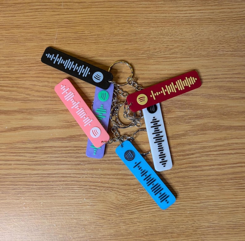 May include: A set of six colorful keychains with a barcode-like design and a small circle in the center. The keychains are attached to a silver key ring.