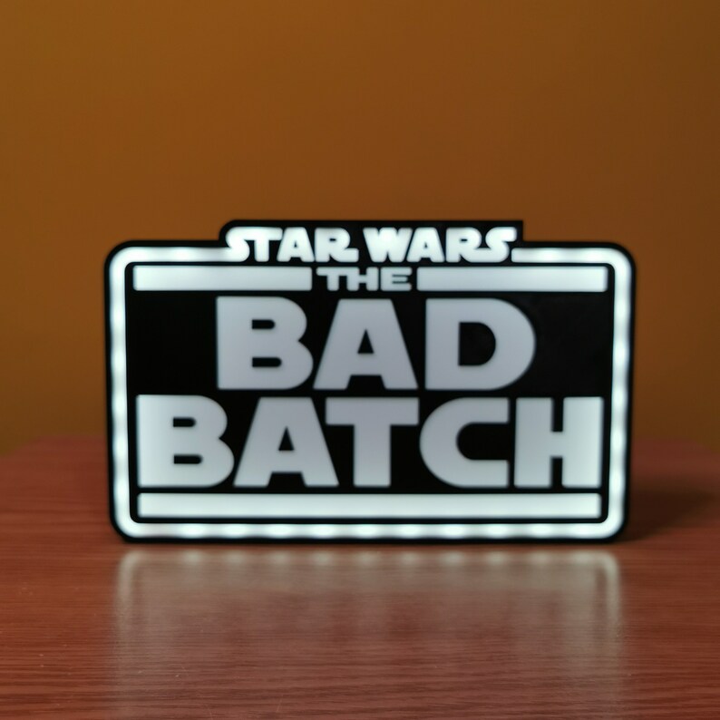 May include: A black and white sign with white LED lights around the border. The sign reads "Star Wars The Bad Batch".