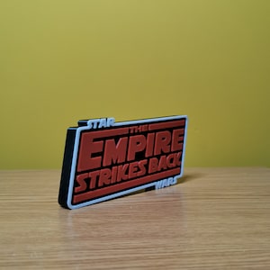 May include: A black and red 3D printed sign with the text "STAR WARS THE EMPIRE STRIKES BACK".