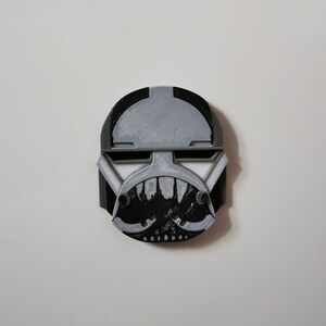 May include: A black and white 3D printed helmet with a menacing, toothy grin. The helmet has a gray top and black details.