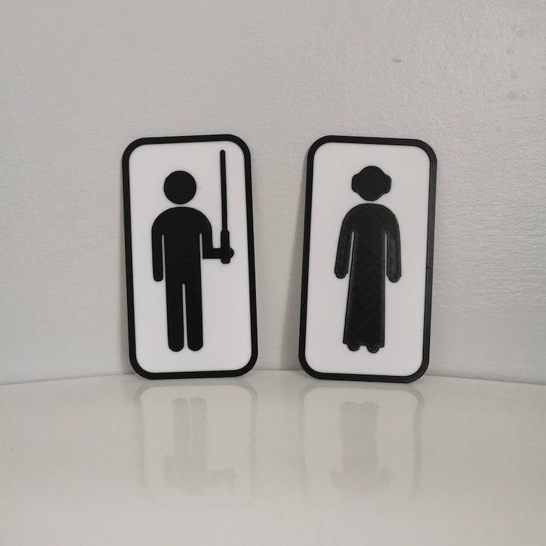 Pu&ograve; includere: Due cartelli da bagno bianchi con bordi neri. Il cartello a sinistra presenta una figura stilizzata che tiene una spada laser. Il cartello a destra presenta una figura stilizzata che indossa una tunica con cappuccio.