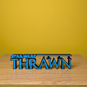 May include: A black and blue 3D printed sign that reads "STAR WARS THRAWN".