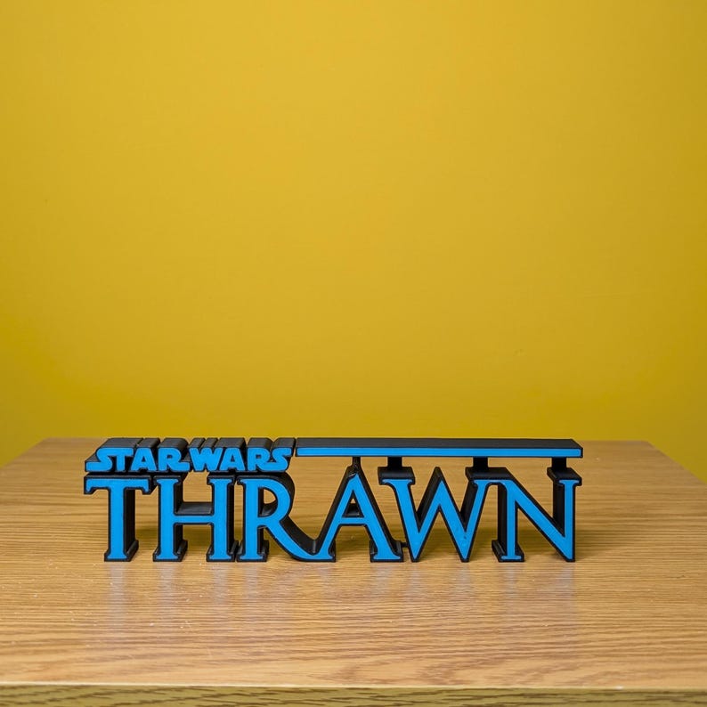 May include: A black and blue 3D printed sign that reads "STAR WARS THRAWN".