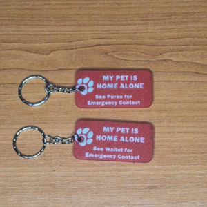 May include: Two red keychains with a paw print and the text "My Pet is Home Alone" with instructions to see the purse or wallet for emergency contact.