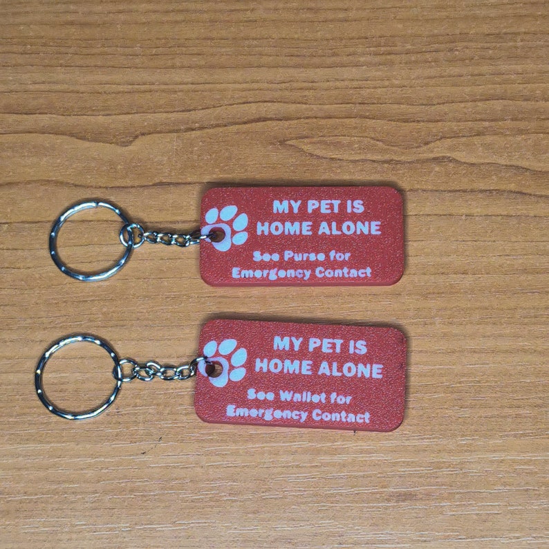 May include: Two red keychains with a paw print and the text "My Pet is Home Alone" with instructions to see the purse or wallet for emergency contact.