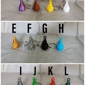 May include: Twelve colourful gnome keychain charms with silver key rings. The gnomes are in various colours, including purple, orange, yellow, white, gold, silver, black, blue, grey, green, red, and teal.