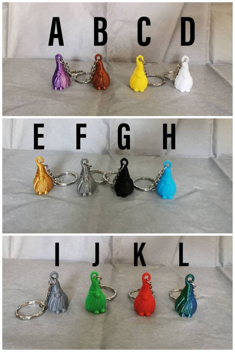 May include: Twelve colourful gnome keychain charms with silver key rings. The gnomes are in various colours, including purple, orange, yellow, white, gold, silver, black, blue, grey, green, red, and teal.