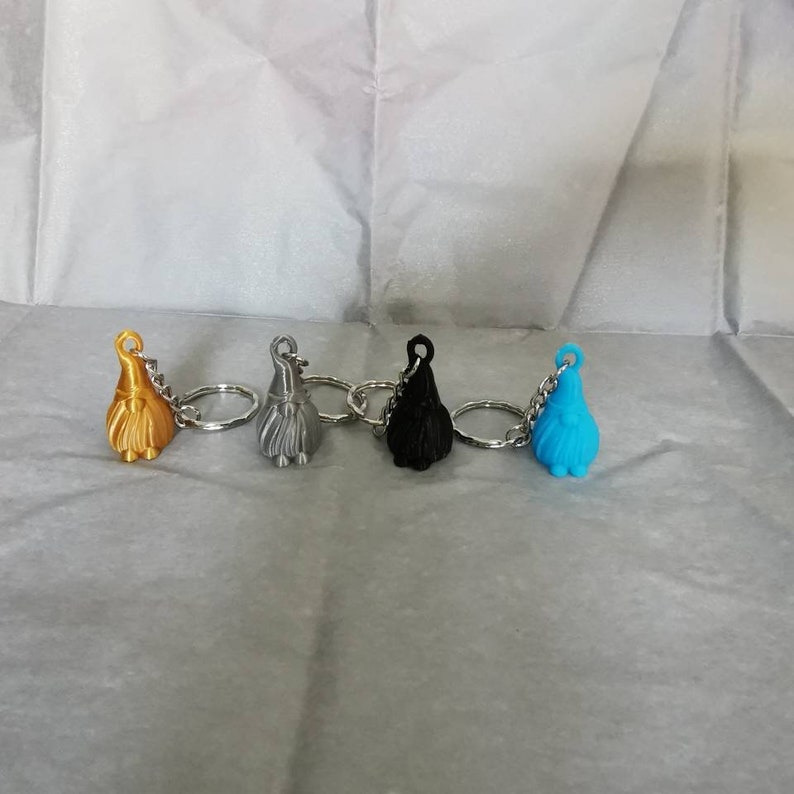 May include: Four gnome keyrings in different colours: gold, silver, black, and blue. Each gnome has a white beard and a red hat.