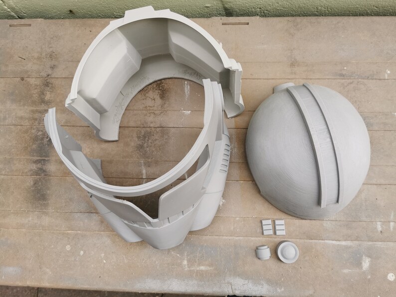 May include: A gray plastic helmet in multiple pieces, including a dome, a front piece, and two side pieces. There are also several small gray plastic pieces.