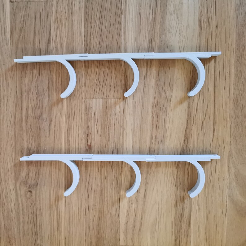 May include: Two white plastic hooks with three hooks each. The hooks are designed to hang items on a wall or other surface.