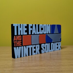 May include: Black and white block with the text "The Falcon and the Winter Soldier" in white letters. The block has a red, white, and blue design with a star.