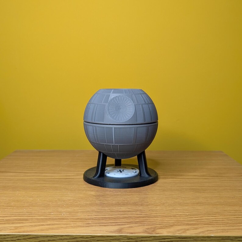 May include: A gray, spherical Death Star model with a black base and three legs. The model is made of plastic and has a detailed design.