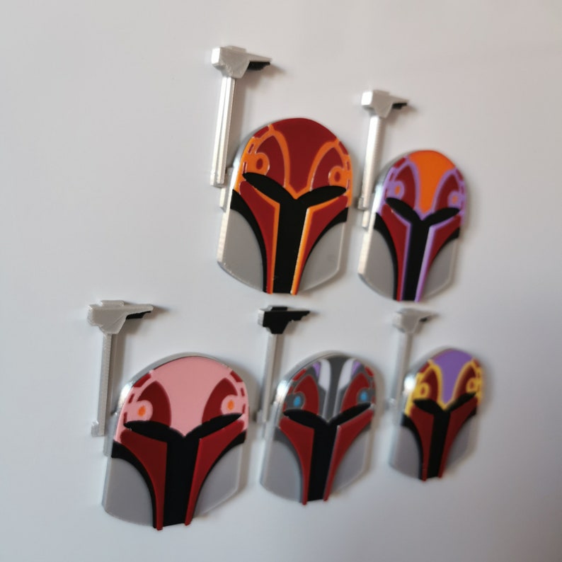 May include: Six Mandalorian helmet magnets in various colors, including red, orange, pink, purple, gray, and black. Each helmet has a silver stand.