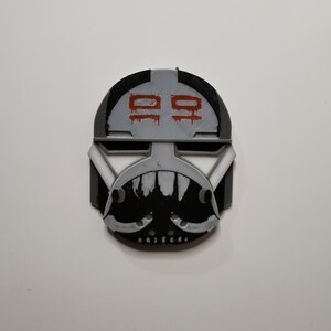 May include: A 3D printed black and white helmet with a red and white symbol on the front. The symbol is a stylized "99".