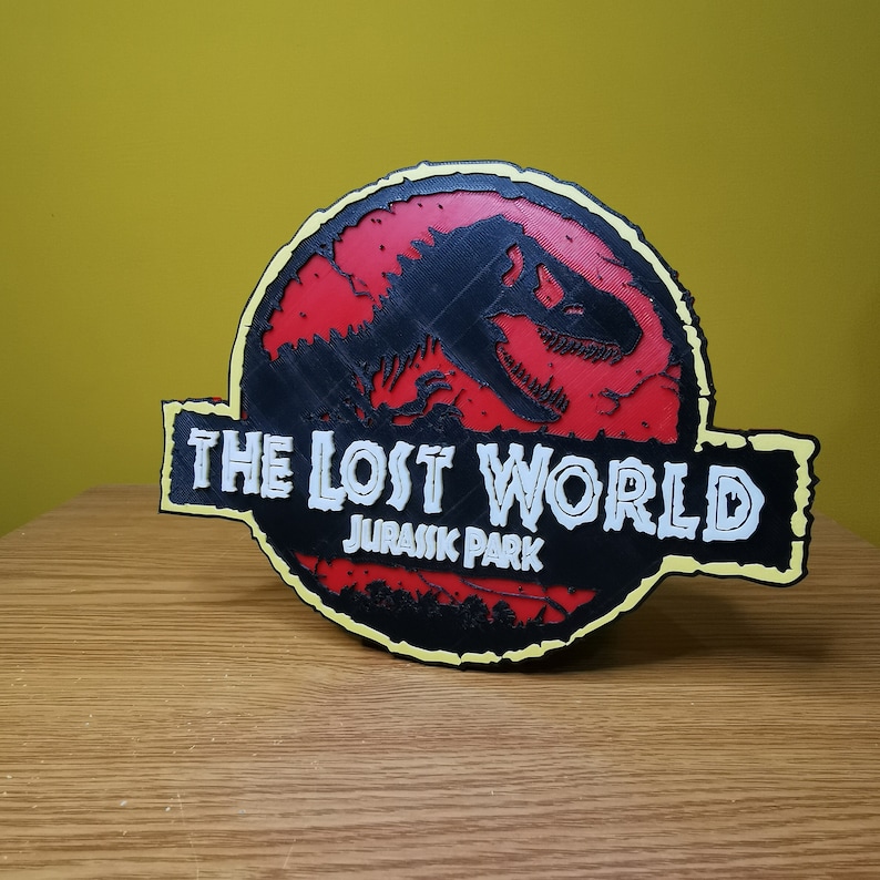 May include: A black and red 3D printed sign with the text "The Lost World Jurassic Park" in white. The sign features a silhouette of a dinosaur.