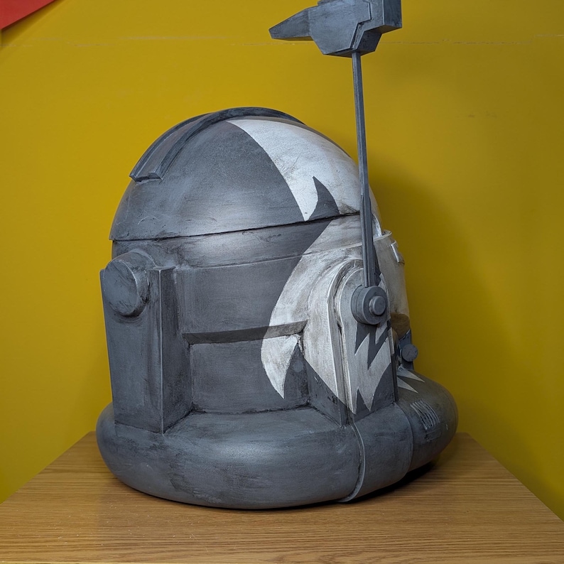 May include: A gray and white helmet with a black and white pattern. The helmet has a small antenna on top.
