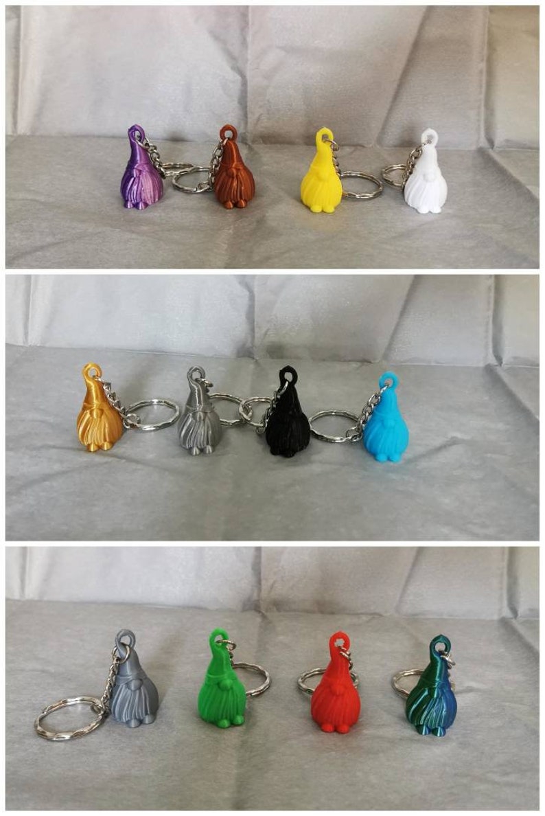 May include: A set of 10 colourful gnome keychain ornaments. The gnomes are made of plastic and have a variety of colours, including purple, brown, yellow, white, gold, silver, black, blue, green, and red. Each gnome has a small beard and a pointy hat.