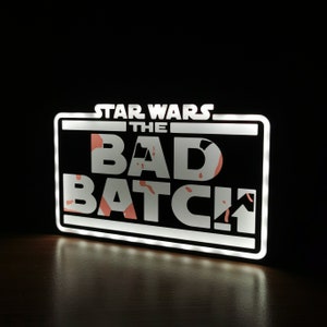 May include: White light-up sign with black background and white text that reads "Star Wars: The Bad Batch". The text has a pink and white splatter pattern.