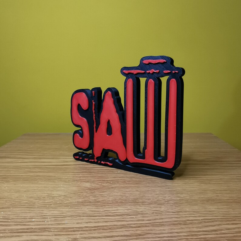 May include: A black and red 3D printed sign that says "SAW" with a trash can icon next to it.
