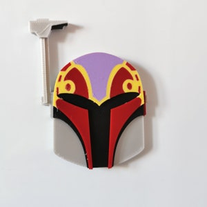 May include: A 3D printed Mandalorian helmet with a red, black, and gold design. The helmet has a purple top and a white antenna.