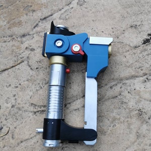 May include: A blue and silver toy blaster with a black handle and a silver barrel. The blaster has a red button and a gold accent.