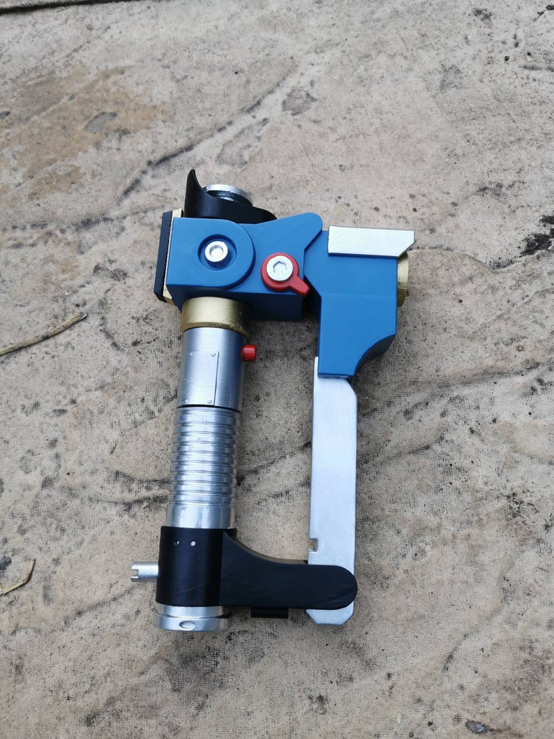 May include: A blue and silver toy blaster with a black handle and a silver barrel. The blaster has a red button and a gold accent.