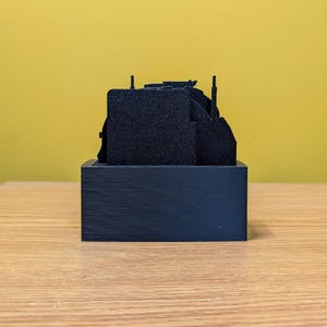 May include: A black 3D printed model of a city skyline, with multiple buildings and towers, on a black base.