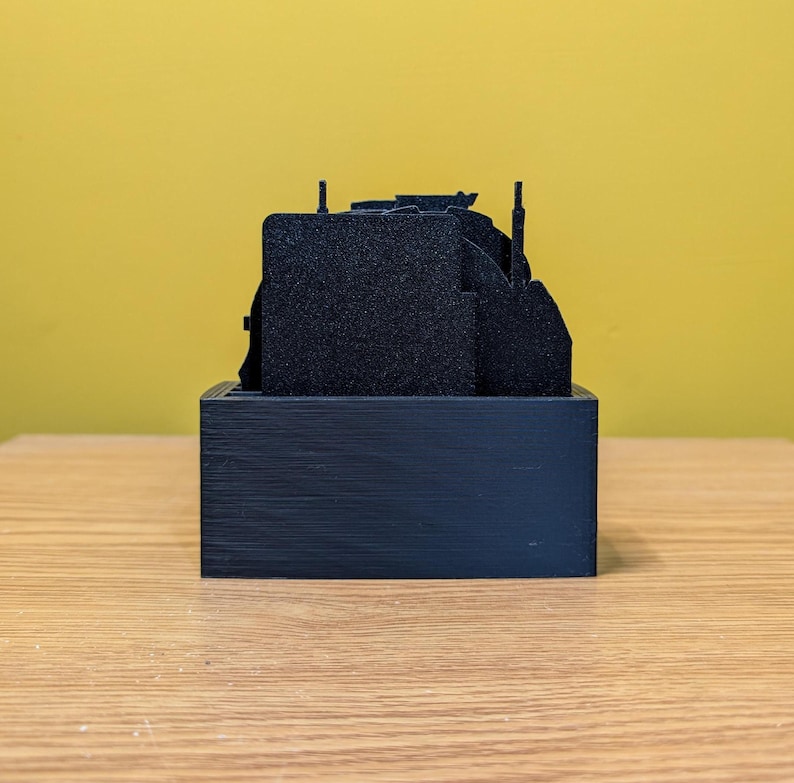 May include: A black 3D printed model of a city skyline, with multiple buildings and towers, on a black base.