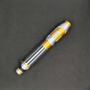 May include: A silver and gold lightsaber toy with a black handle. The lightsaber is about 12 inches long.